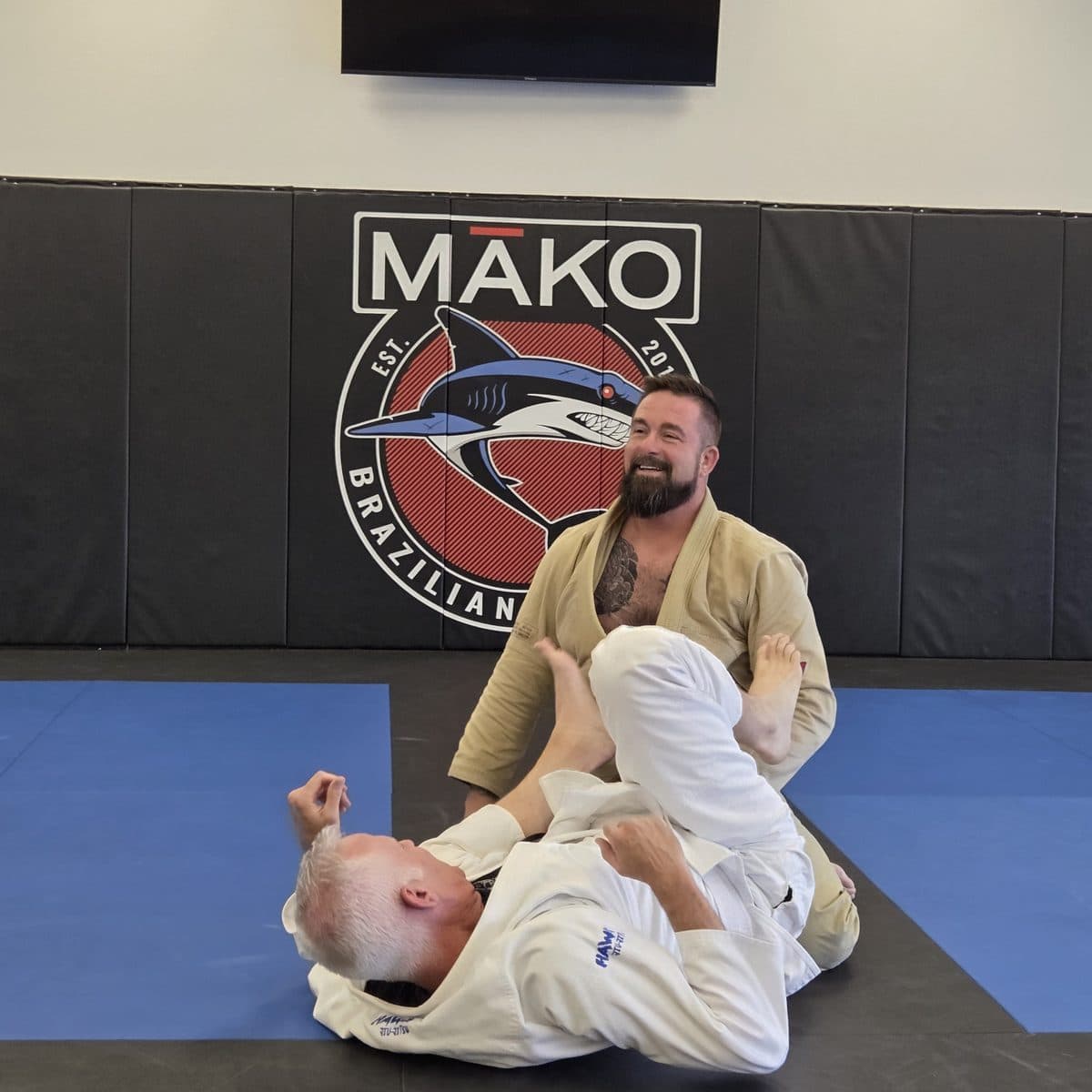 Two officers in gis working a guard position on the mat at a partner academy